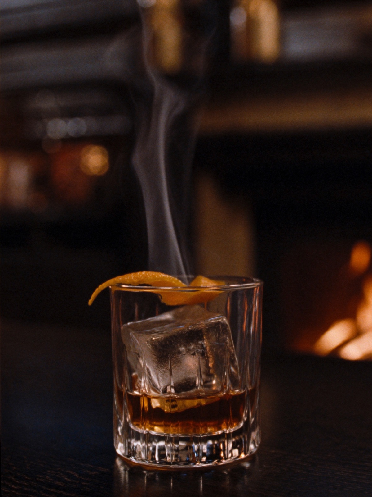 A smoked Old Fashioned with an orange peel, smoke rising from the glass.