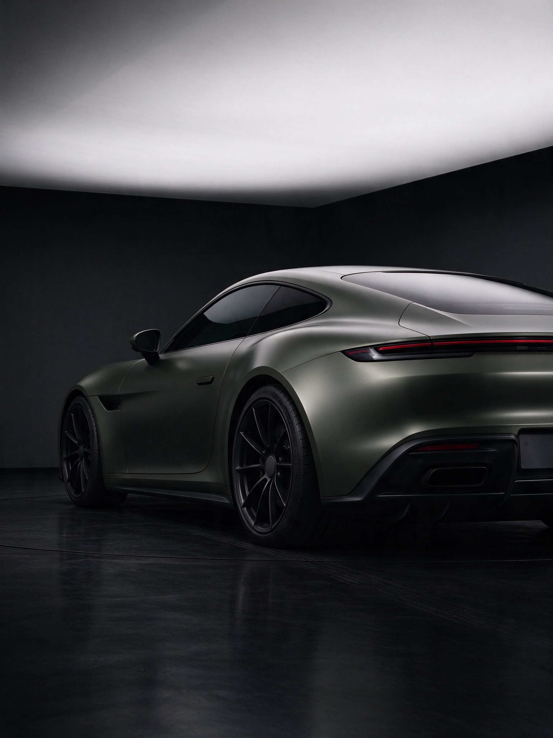 A sports coupe wrapped in satin olive, parked in a dark studio under a white light panel.